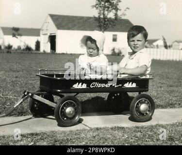 Authentique photographie vintage des années 1950 de deux enfants dans Clipper Wagon, banlieue arrière-cour - Noir et blanc Mid-Century American Childhood Nostalgia Banque D'Images