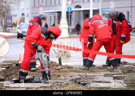 Travailleurs répare la surface du trottoir, travailleurs avec un marteau-piqueur. Groupe d'hommes en uniforme dans la rue de la ville au printemps Banque D'Images