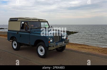 FELIXSTOWE, SUFFOLK, ANGLETERRE - 01 MAI 2022 : un classique Blue Land Rover conduit le long de la promenade de bord de mer sur l'océan en arrière-plan. Banque D'Images