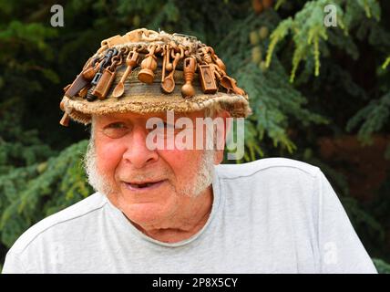 OXBOROUGH, NORFOLK, ANGLETERRE - 12 JUILLET 2022: Homme plus âgé avec chapeau sur lequel est recouvert de cuillères d'amour en bois sculpté. Banque D'Images