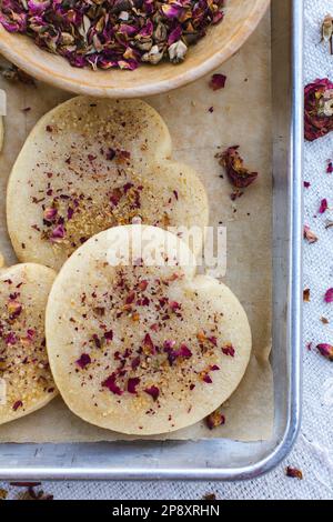 Biscuits en forme de coeur sur un plateau parsemé de pétales de rose. Banque D'Images