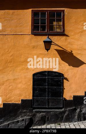 Un lampadaire mural sur un bâtiment résidentiel avec des murs jaunes au soleil. Ancienne porte en métal noire. Banque D'Images