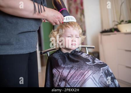 Une petite fille maurie aux cheveux blonds dans un salon de beauté. Coupes de cheveux pour enfants. Salon de coiffure pour enfants. Coupe de cheveux de fille à la maison Banque D'Images