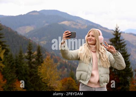 Jeune femme en casque chaud prenant le selfie le jour de l'automne Banque D'Images