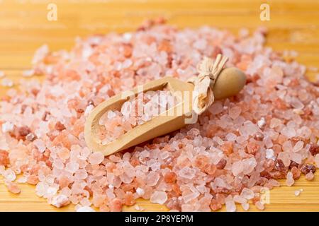 Une image rapprochée d'une petite pelle en bois sur une pile de sel de mer de l'Himalaya rose cru dans une photo de studio. Banque D'Images