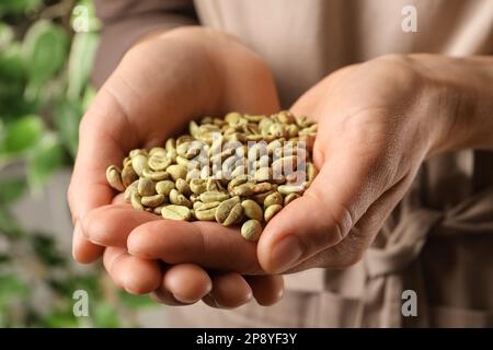 Femme tenant une pile de grains de café verts sur fond flou, gros plan Banque D'Images