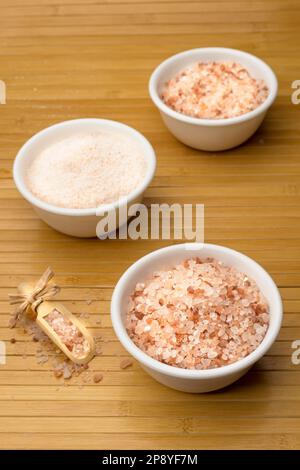 Une photo en gros plan de sel de mer himalayan rose à grain grossier et fin avec une pelle en bois sur le côté. Banque D'Images