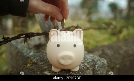 Un moment de mettre une pièce dans Pink Piggy Bank à l'extérieur Banque D'Images