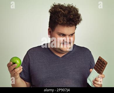 J'ai fait mon choix. un homme en surpoids décidant entre une pomme et une barre de chocolat. Banque D'Images