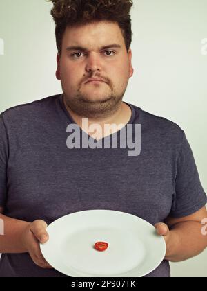 Vous devez me plaisanter. Portrait d'un homme en surpoids tenant une assiette avec une petite bande de tomate. Banque D'Images