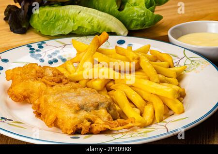Vue imprenable sur de délicieux poissons cuits faits maison et frits français dans un plat en céramique blanche avec une tasse de sauce maison et légumes verts frais sur le wo Banque D'Images