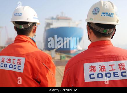 QINGDAO, CHINE - le 10 MARS 2023 - deux dockers observent qu'une usine modulaire de GNL quitte le quai de Qingdao, dans la province de Shandong, en Chine, au 10 mars 2023. Banque D'Images