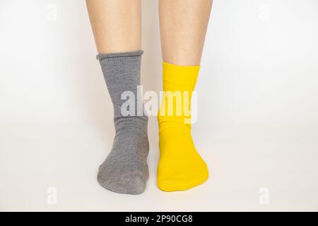 Les jambes des femmes dans différentes chaussettes, l'un est bleu et l'autre est jaune sur un fond blanc, mode Banque D'Images