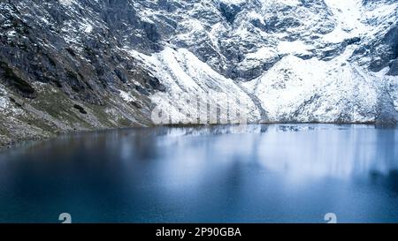 Czarny Staw Pod Rysamy ou lac Black Pond près de la cabane de montagne Morskie Oko Snowy dans les montagnes polonaises de Tatry, vue sur les drones, Zakopane, Pologne. Vue aérienne prise de magnifiques collines verdoyantes et montagnes dans des nuages sombres et reflet sur le lac Morskie Oko. Destination touristique de voyage Banque D'Images