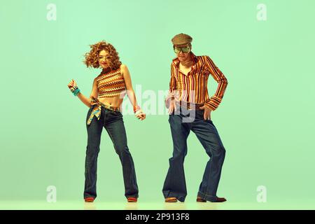 Danse incendiaire. Homme et femme émotif en vêtements rétro dansant danse disco sur fond vert. Concept des tendances de la mode de 70s, 1980s Banque D'Images