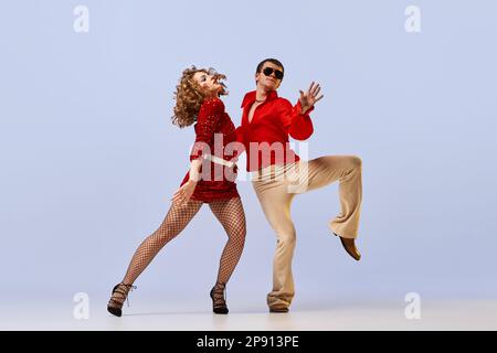 Danse de salle de bal disco. Couple expressif de danseurs dans des vêtements de mode rétro lumineux, costumes de scène dansant sur fond de couleur lilas. Concept de Banque D'Images