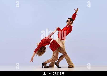 Danse de salle de bal disco. Couple expressif de danseurs dans des vêtements de mode rétro lumineux, costumes de scène dansant sur fond de couleur lilas. Concept de Banque D'Images