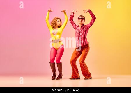 Elégant et expressif couple de danseurs professionnels dans des vêtements rétro danse disco danse sur fond rose-jaune. Banque D'Images