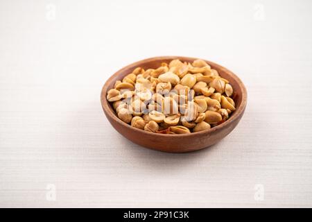 Grains de cacahuètes aromatisés épicés dans un bol sur fond de table blanc. Banque D'Images