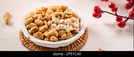 Grains de cacahuètes aromatisés épicés dans un bol sur fond de table blanc. Banque D'Images