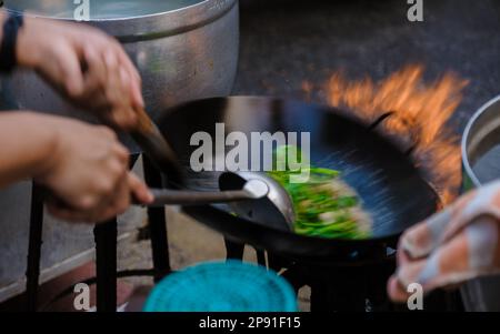 Bangkok Ratchawat Thailand les gens préparent la nourriture de rue thaï dans une cabine de nourriture avec un wok poêle faire sauter les légumes. peu de flou grâce aux mouvements rapides Banque D'Images