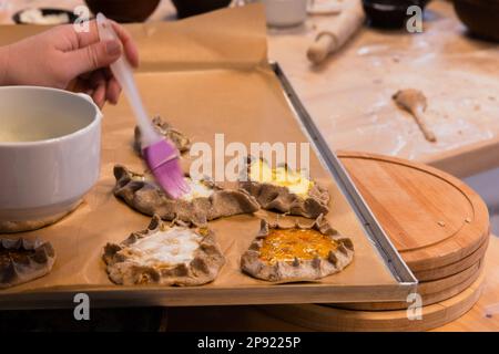 Préparation des pâtisseries maison de Karelian au four, brossage avec du beurre fondu, gros plan avec une mise au point douce sélective Banque D'Images