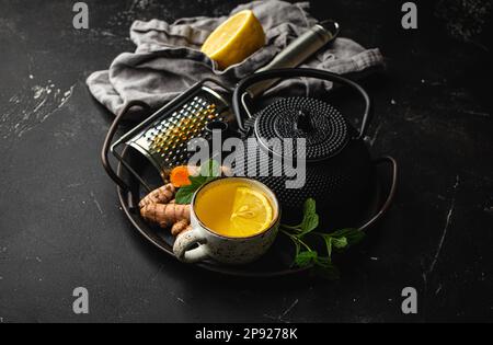 Thé curcuma à base de plantes chaud et sain pour stimuler le système immunitaire. Ingrédients pour faire du thé de détox dans une tasse, théière noire, racine de curcuma fraîche, citron, menthe Banque D'Images