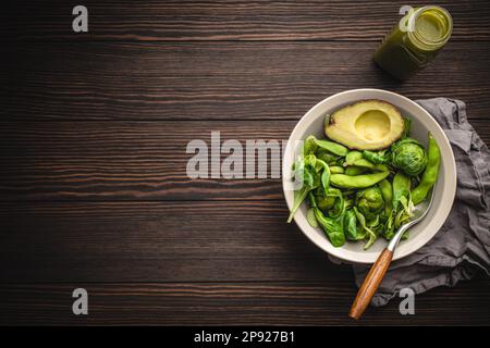 Salade verte saine aux épinards, choux de bruxelles, avocat dans un bol et smoothie de detox vert dans une bouteille sur fond de bois, vue du dessus. Aliments crus Banque D'Images