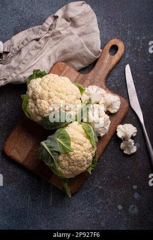 Chou-fleur frais de coupe biologique sur planche à découper en bois avec couteau de cuisine, prêt à être cuit, vue du dessus avec espace de copie. Nourriture végétarienne, manger propre Banque D'Images