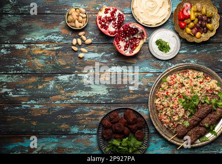 Divers plats turcs: Kebab de viande avec salade de tabouleh, falafel, houmous, olives, pistaches et meze du Moyen-Orient sur table en bois avec vue Banque D'Images