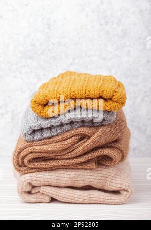 Pile de vêtements, chandails et casquettes tricotés chauds sur fond de bois blanc rustique. Pile de tricots pliés et confortables, concept capsule de garde-robe d'hiver Banque D'Images