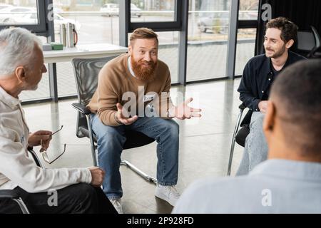 Homme gai avec la dépendance à l'alcool parlant au groupe interracial dans le centre de réadaptation, image de stock Banque D'Images