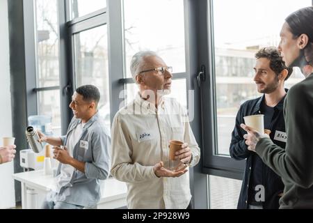 Homme mature avec dépendance à l'alcool tenant une tasse de papier et parlant aux gens dans le centre de récupération, image de stock Banque D'Images