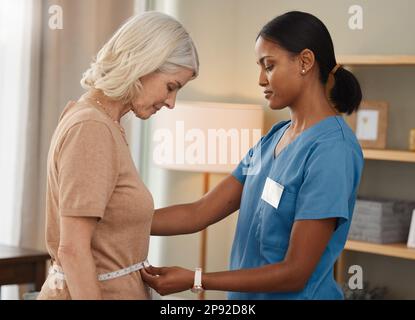 Ce qui est mieux que de manger Un régime thats médecin approuvé. Prise de vue d'un médecin à l'aide d'un ruban de mesure sur l'estomac d'une femme âgée lors d'une consultation à Banque D'Images