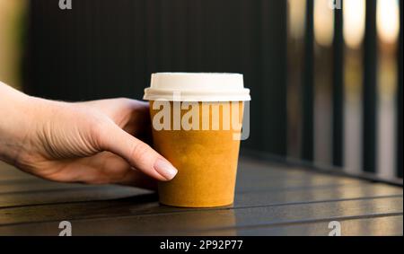 mains de womans pour un café en papier avec couvercle blanc. Café véranda avec table ouverte Banque D'Images