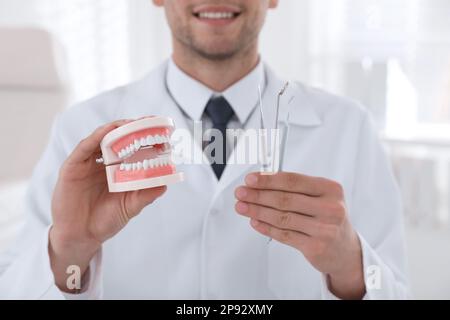 Dentiste tenant le modèle de mâchoires et les outils en clinique, gros plan Banque D'Images