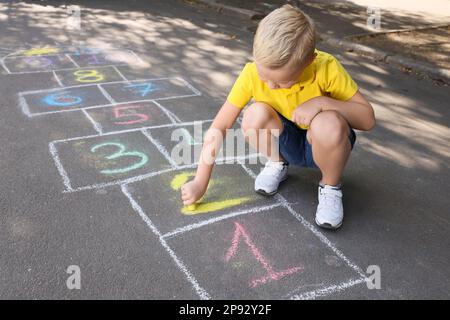 Petit garçon dessin hopscotch avec de la craie sur l'asphalte à l'extérieur. Bonne enfance Banque D'Images