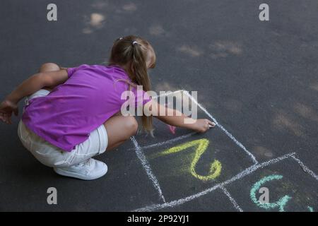 Petite fille dessin hopscotch avec craie sur l'asphalte à l'extérieur. Bonne enfance Banque D'Images