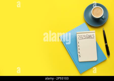 Inscription 2023 objectifs écrits en cahier, stylo et café sur fond jaune, plat avec espace pour le texte. Objectifs de la nouvelle année Banque D'Images