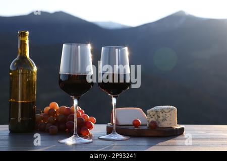 Vin rouge servi avec du fromage et des raisins sur une table en bois, dans le paysage montagneux Banque D'Images