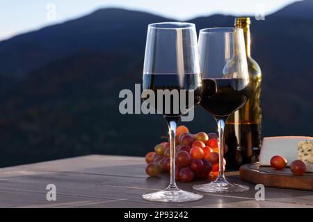 Vin rouge servi avec du fromage et des raisins sur une table en bois, dans le paysage montagneux Banque D'Images
