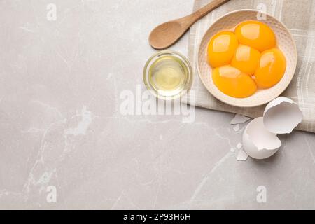 Composition de la couche plate avec jaunes d'œufs crus et blancs sur une table en marbre gris clair, espace pour le texte Banque D'Images
