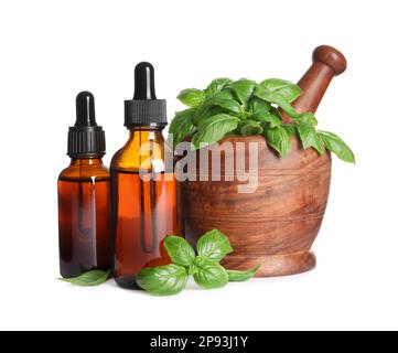 Bouteilles d'huile essentielle de basilic près du mortier en bois avec feuilles et pilon sur fond blanc Banque D'Images