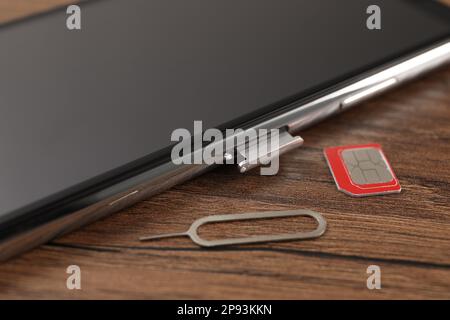 Carte SIM, téléphone portable et outil d'éjection sur table en bois, gros plan Banque D'Images