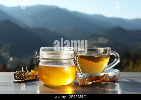 Miel frais aromatique et tasse de thé chaud sur une table en bois gris au milieu des montagnes Banque D'Images