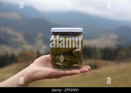 Femme tenant un pot de délicieux concombres marinés dans les montagnes, en gros plan Banque D'Images