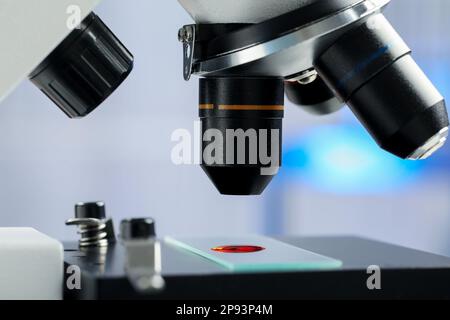 Lame de verre avec échantillon de liquide rouge sous microscope en laboratoire, gros plan Banque D'Images