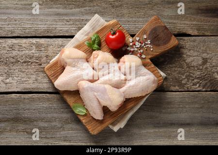 Ailes de poulet crues avec basilic, tomate et épices sur une table en bois, vue du dessus Banque D'Images