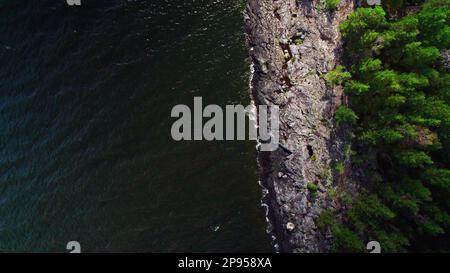 Le soleil brille sur les rochers, les forêts et l'eau et le lac est éclipsé par des nuages sombres. Vue aérienne à grand angle Lac de Vanern Varmland Suède Banque D'Images