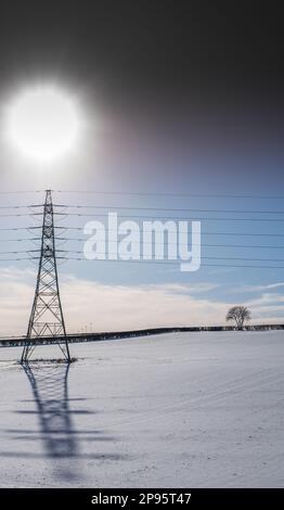 Lignes de transmission de câbles aériens haute tension fonctionnant à 275kV avec des isolateurs de verre traversant un champ recouvert de neige avec ombre et soleil. Banque D'Images